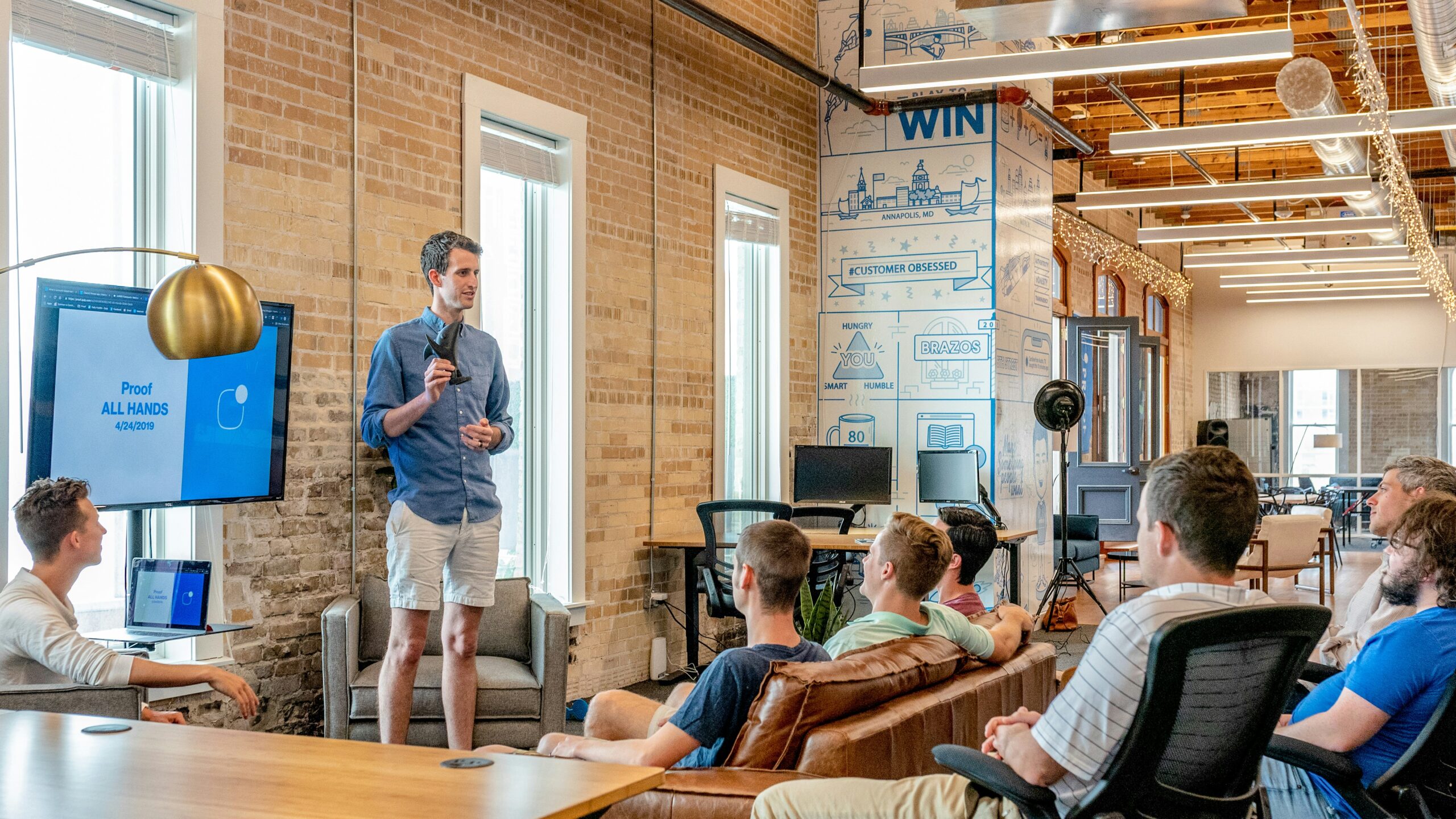 A photograph of a Product Manager giving a talk to a handful of colleagues in an office setting.