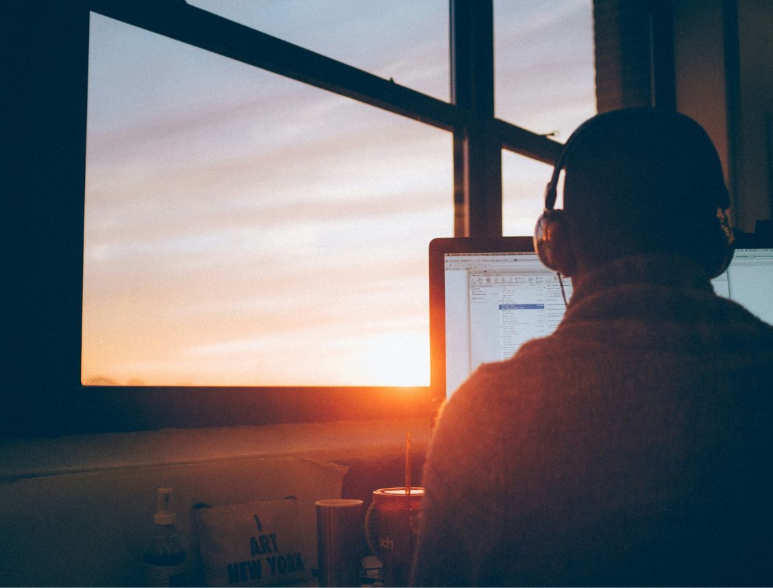 A Product Manager working remotely from home, seated at a desk with a laptop with the sun setting ahead of him.